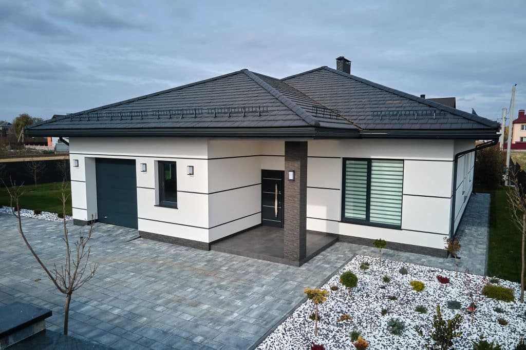 Neues Einfamilienhaus im Landhausstil mit angebauter Garage und großem, gepflastertem, umzäuntem Garten an einem sonnigen Tag in einer modernen Vorstadtgegend.